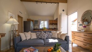 Un salón acogedor con un sofá, una mesita de centro con un libro y un frutero, y una cocina al fondo.