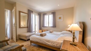 Habitación de hotel con cama doble, mesita de noche con lámpara, una silla, un banco y un espejo grande.