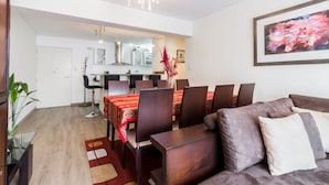 A modern living room with a dining area, a kitchen in the background, and a large painting on the wall. - LUXURY APARTMENT IN MIRAFLORES, LIMA, PERU, 2 BEDROOMS WITH JACUZZI (Miraflores)