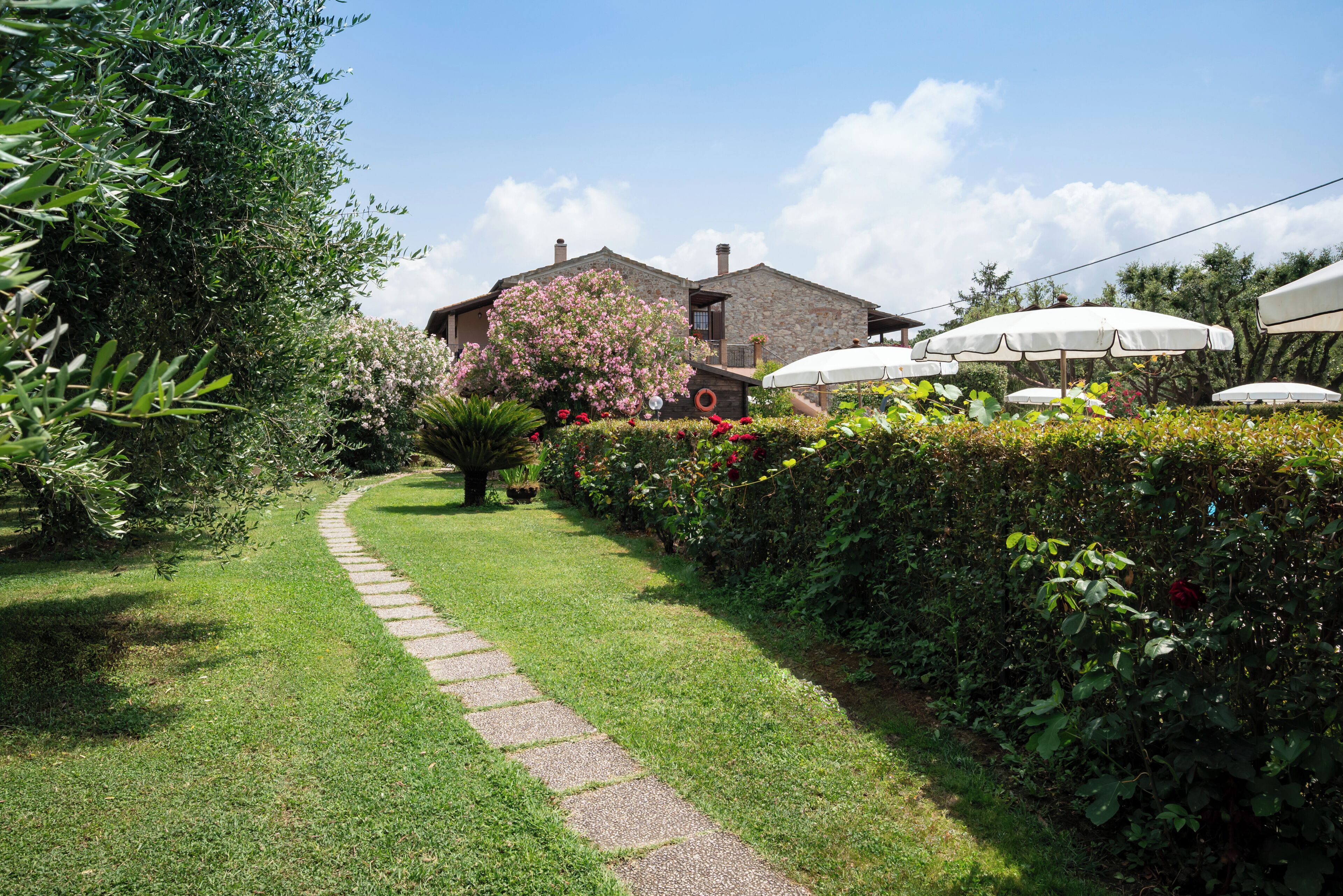 Una casa de piedra con un camino empedrado que lleva a la entrada, rodeada de vegetación exuberante y plantas con flores.