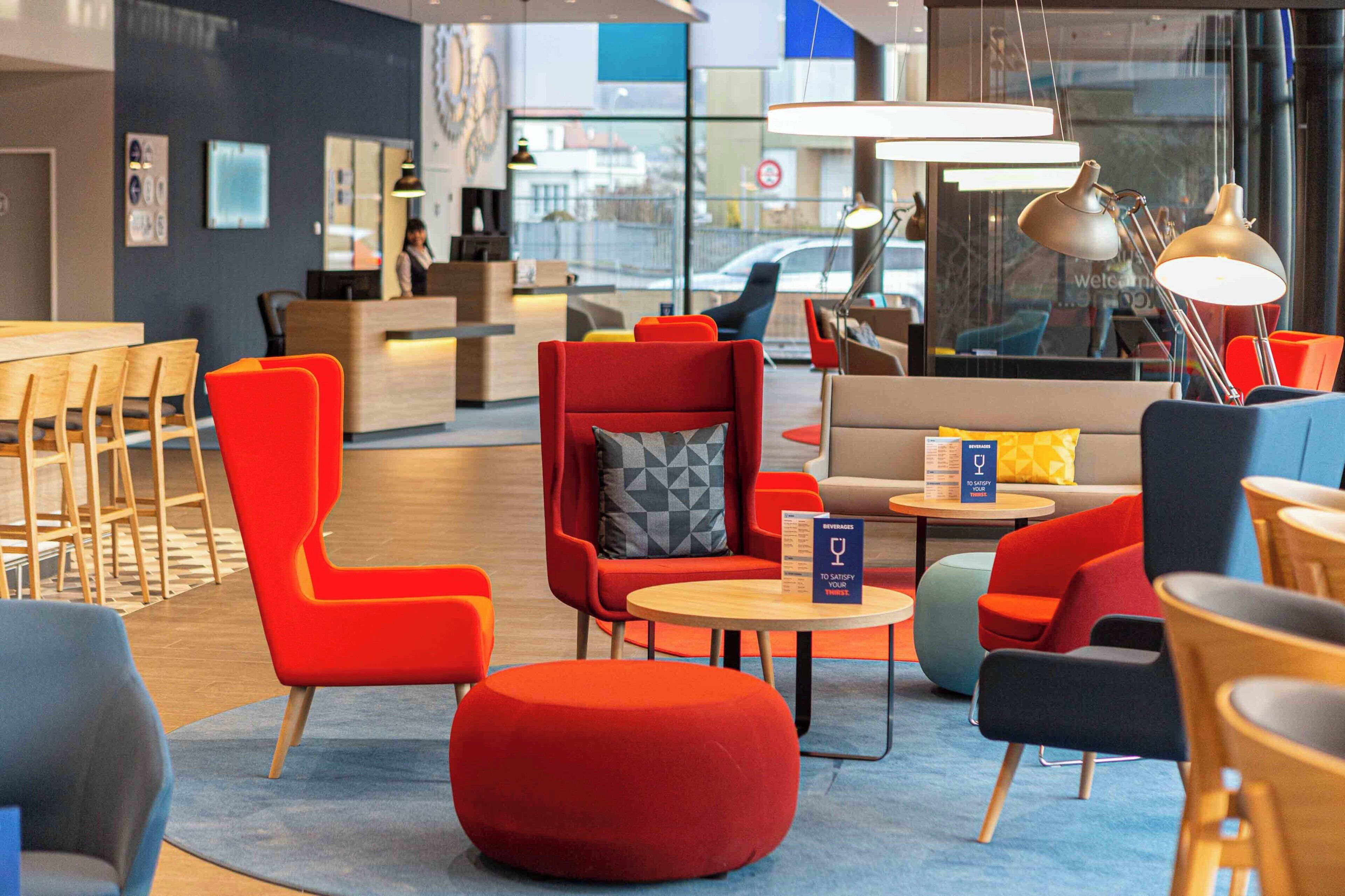 Een moderne lounge met rode en blauwe zitplaatsen, een receptiebalie en een uitzicht op de stad door grote ramen.