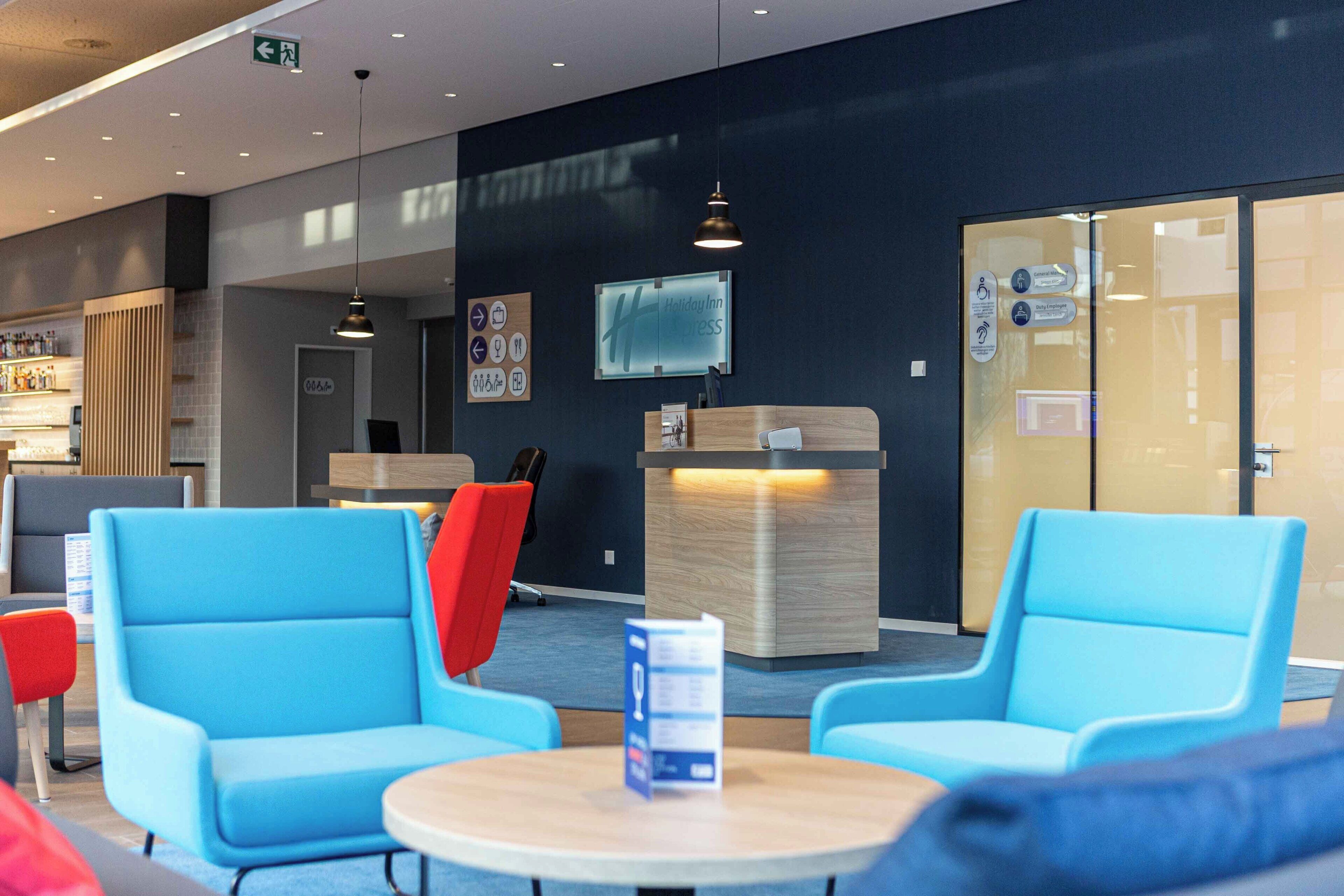 A modern hotel lobby with blue seating, a reception desk, and a glass wall.