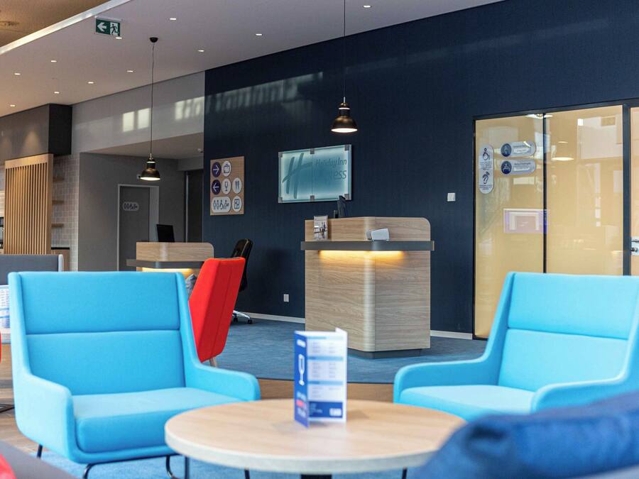 A modern hotel lobby with blue seating, a reception desk, and a glass wall.