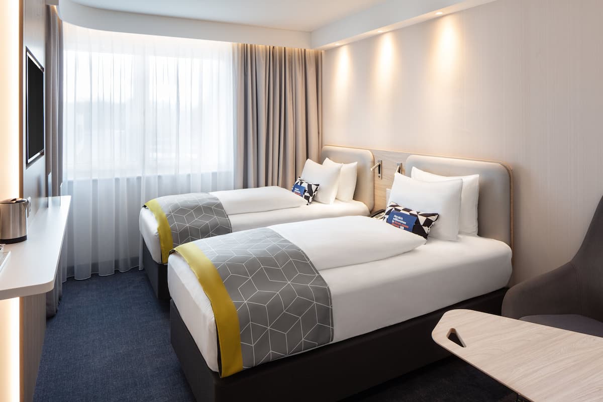 A hotel room with two beds, a desk, and a chair.