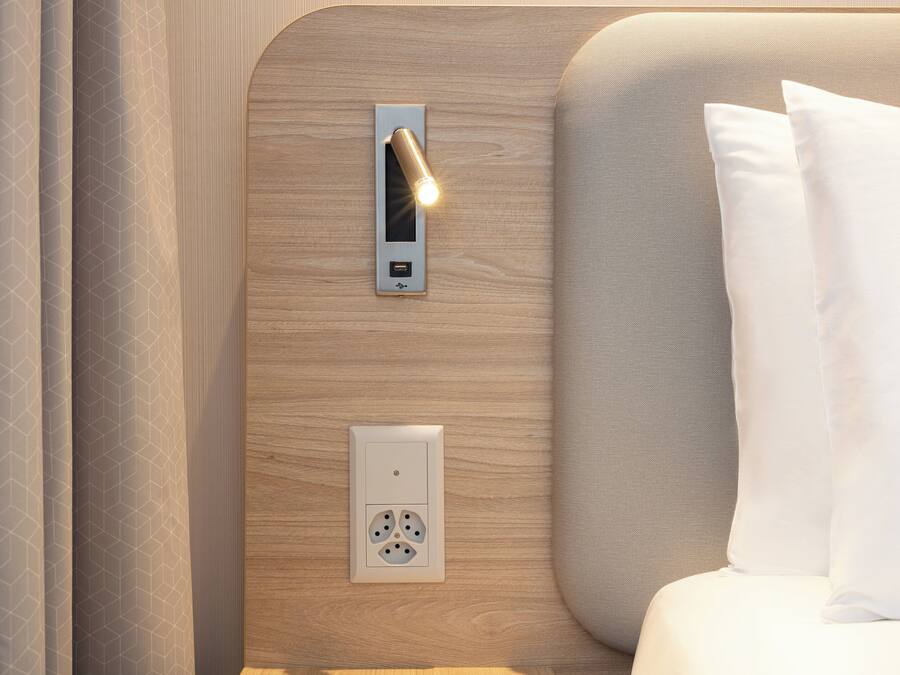 A modern hotel room with a wooden headboard, a bedside table, and a nightstand.