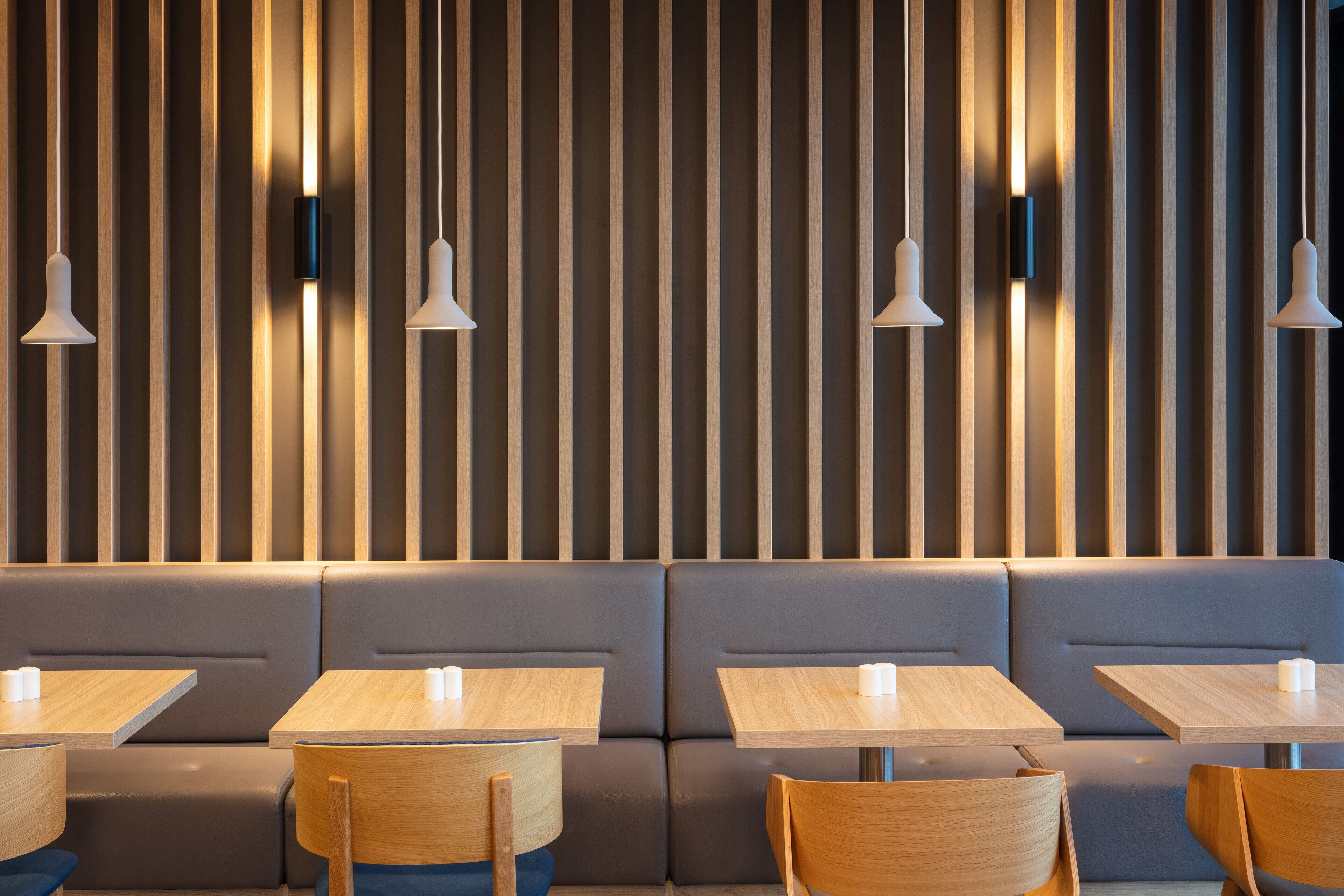 A modern restaurant interior with wooden slats, cushioned seating, and pendant lighting.