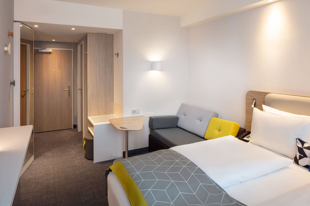A hotel room with a bed, a desk, a chair, and a sofa.