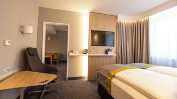 A hotel room with a bed, a desk, a chair, a television, and a bathroom visible through an open door.