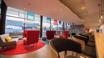 A modern lounge area with red and grey seating, large windows, and a view of the cityscape.