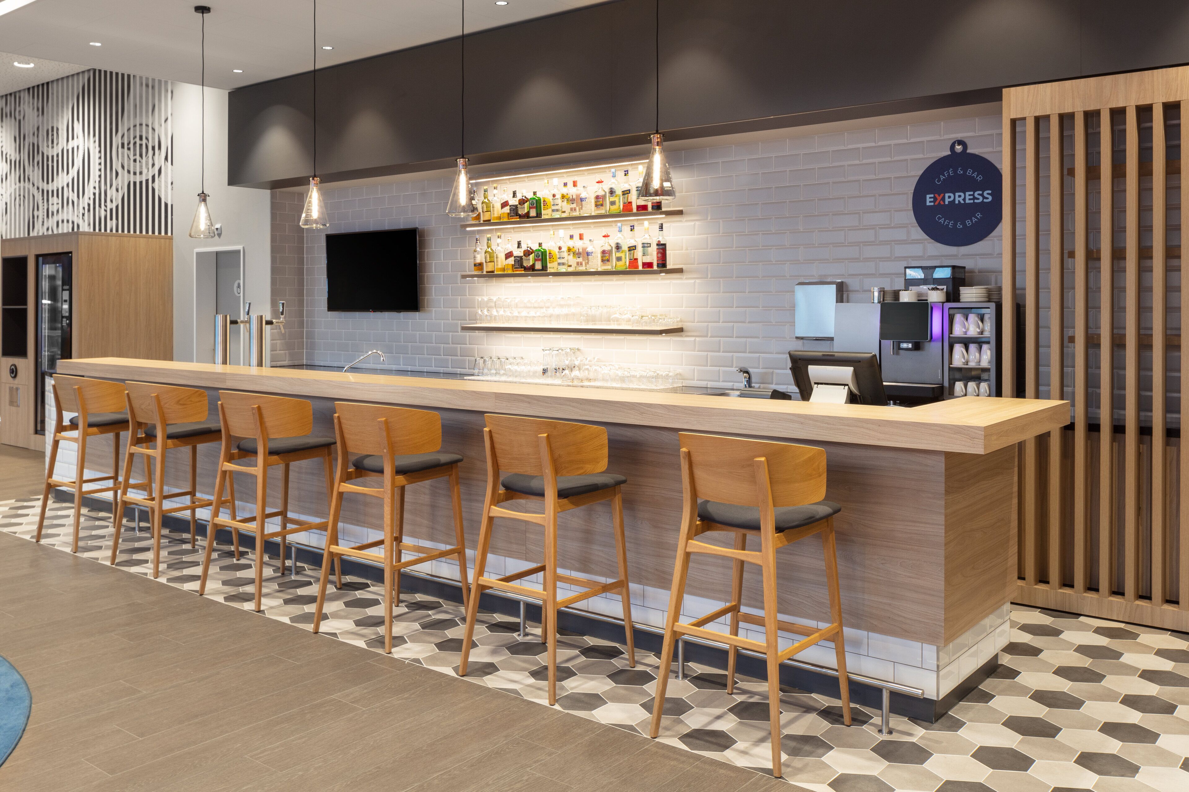 A modern bar area with a long counter, multiple stools, and a variety of bottles on shelves.