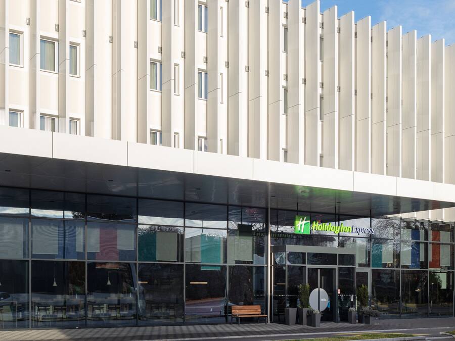 Un hotel moderno con fachada de vidrio, entrada cubierta y cartel de Holiday Inn Express.