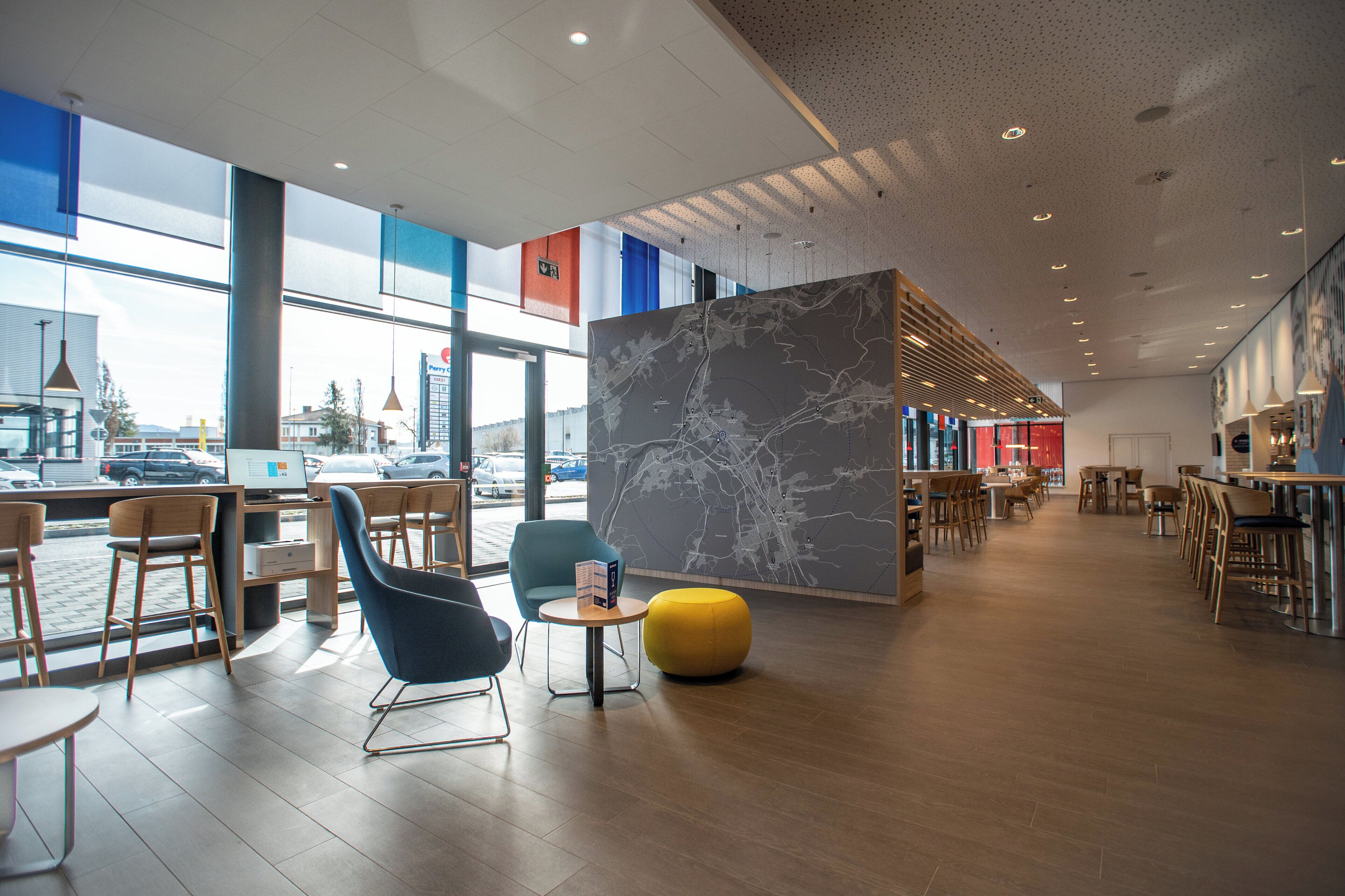 A modern interior with seating areas, a map display, and large windows offering views of the city.