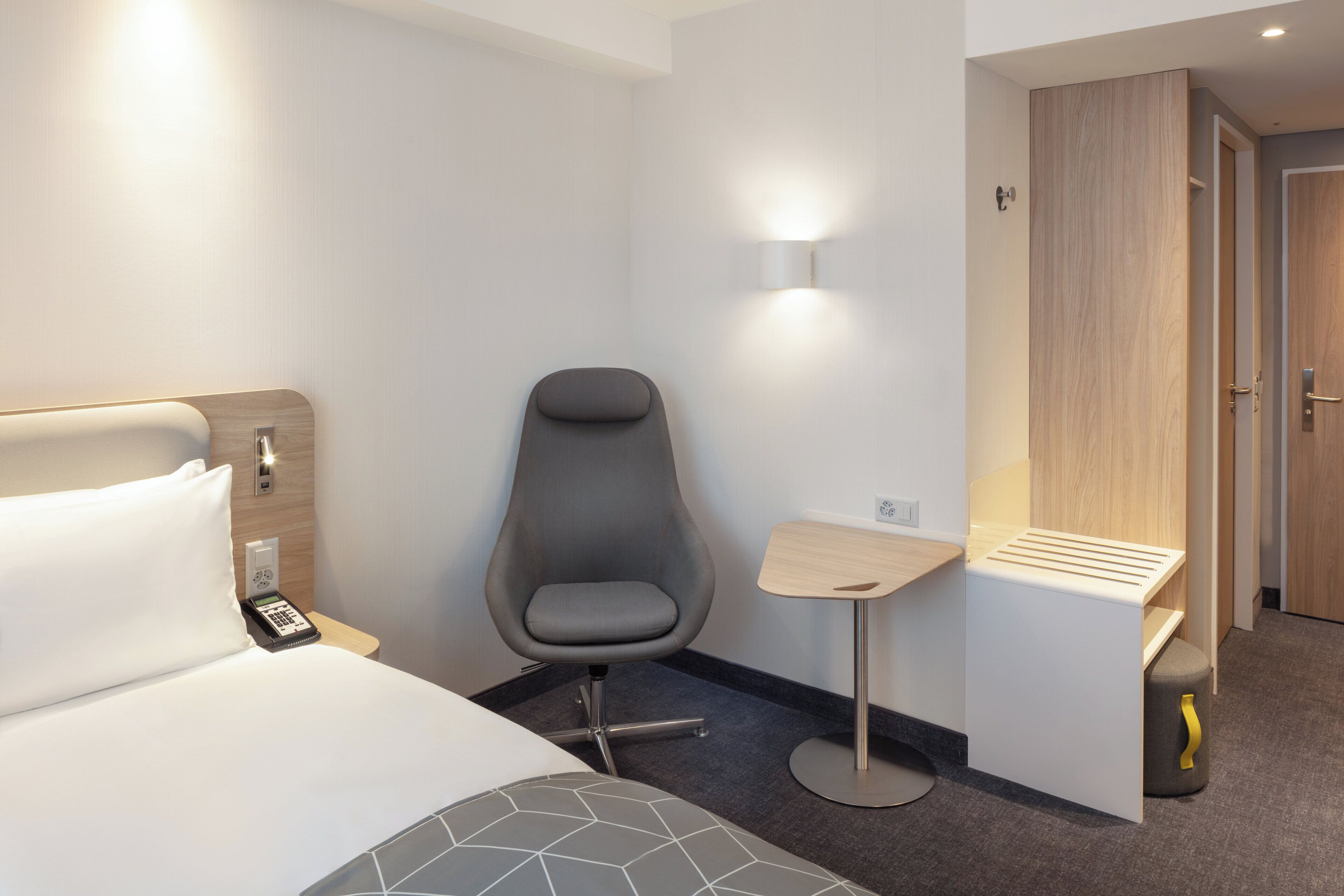 Hotellihuone, jossa on sänky, työpöytä, tuoli, seinään kiinnitetty valaisin ja vaatekaappi.