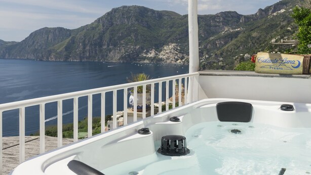 Een jacuzzi op een balkon met uitzicht op een kustlandschap, bergen en een waterpartij.