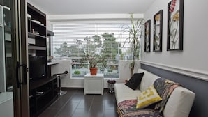 Een woonkamer met een bank, een televisie, een radiator, een potplant en een raam met jaloezieën.