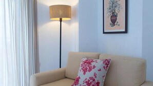 A beige sofa with a floral pillow, a floor lamp, and a framed artwork on the wall.