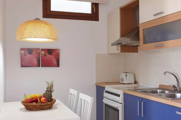 A compact kitchen with a white table, a fruit basket, a toaster, and a stove.