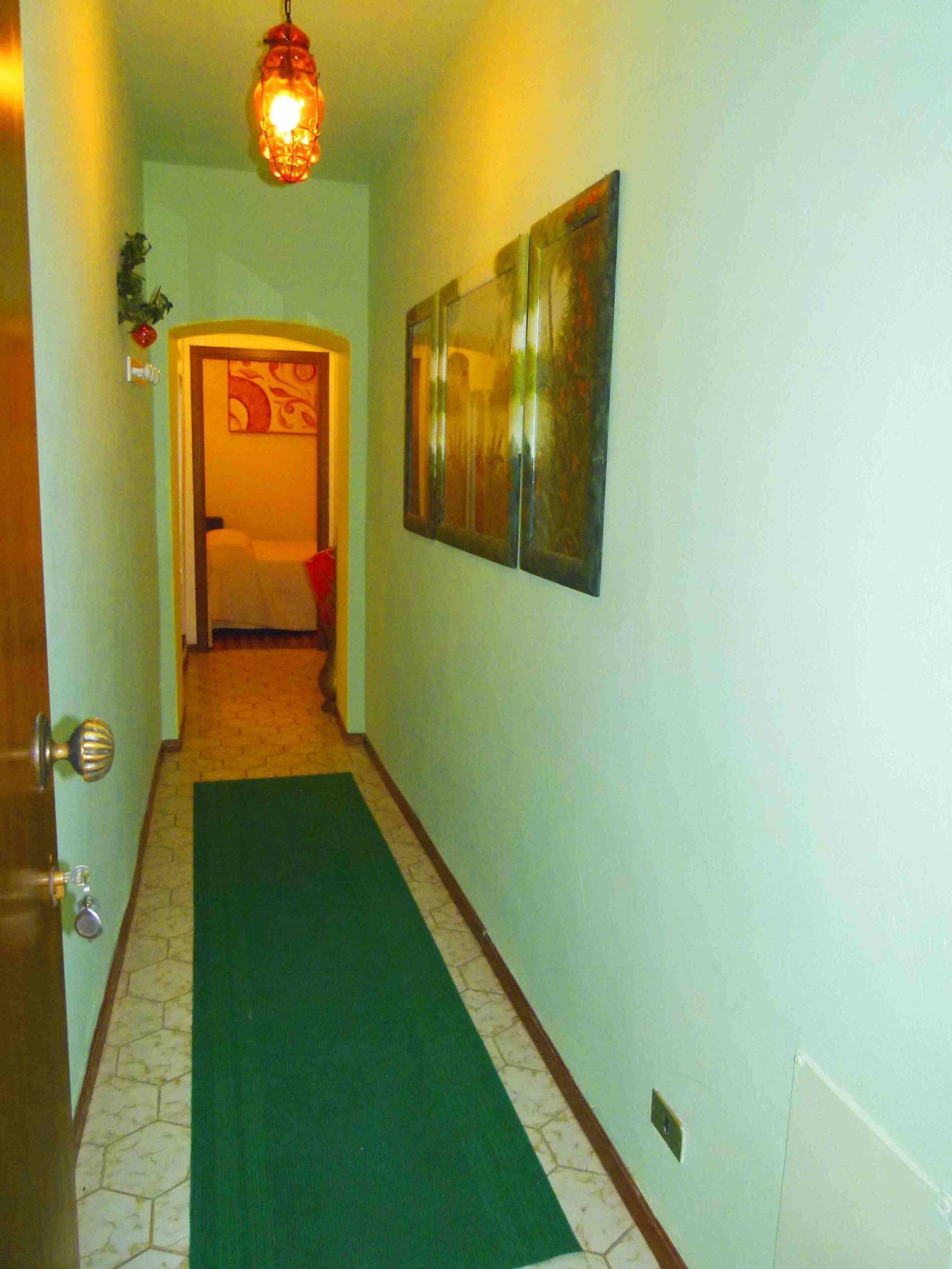 En hall med ett grönt golv, en dörr med ett mässingshandtag och en väggmonterad lampa.