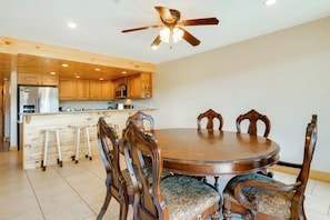 A dining area with a round wooden table and ornate chairs, a kitchen with wooden cabinets, and a ceiling fan.