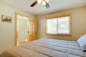 Une chambre à coucher avec un lit, une fenêtre avec des stores, un ventilateur de plafond et une porte.