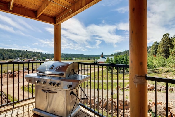 Un barbecue sur un balcon, avec vue sur le clocher d’une église et sur des collines boisées.