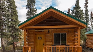 A log cabin with a green roof, a wooden porch, and a staircase leading to the entrance. - Cozy Bear Log Cabin Tri-Valley  (Healy)