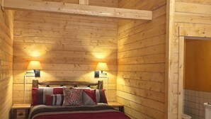 A wooden cabin bedroom with a bed, two bedside lamps, and a visible bathroom with a toilet. - Cozy Bear Log Cabin Tri-Valley  (Healy)