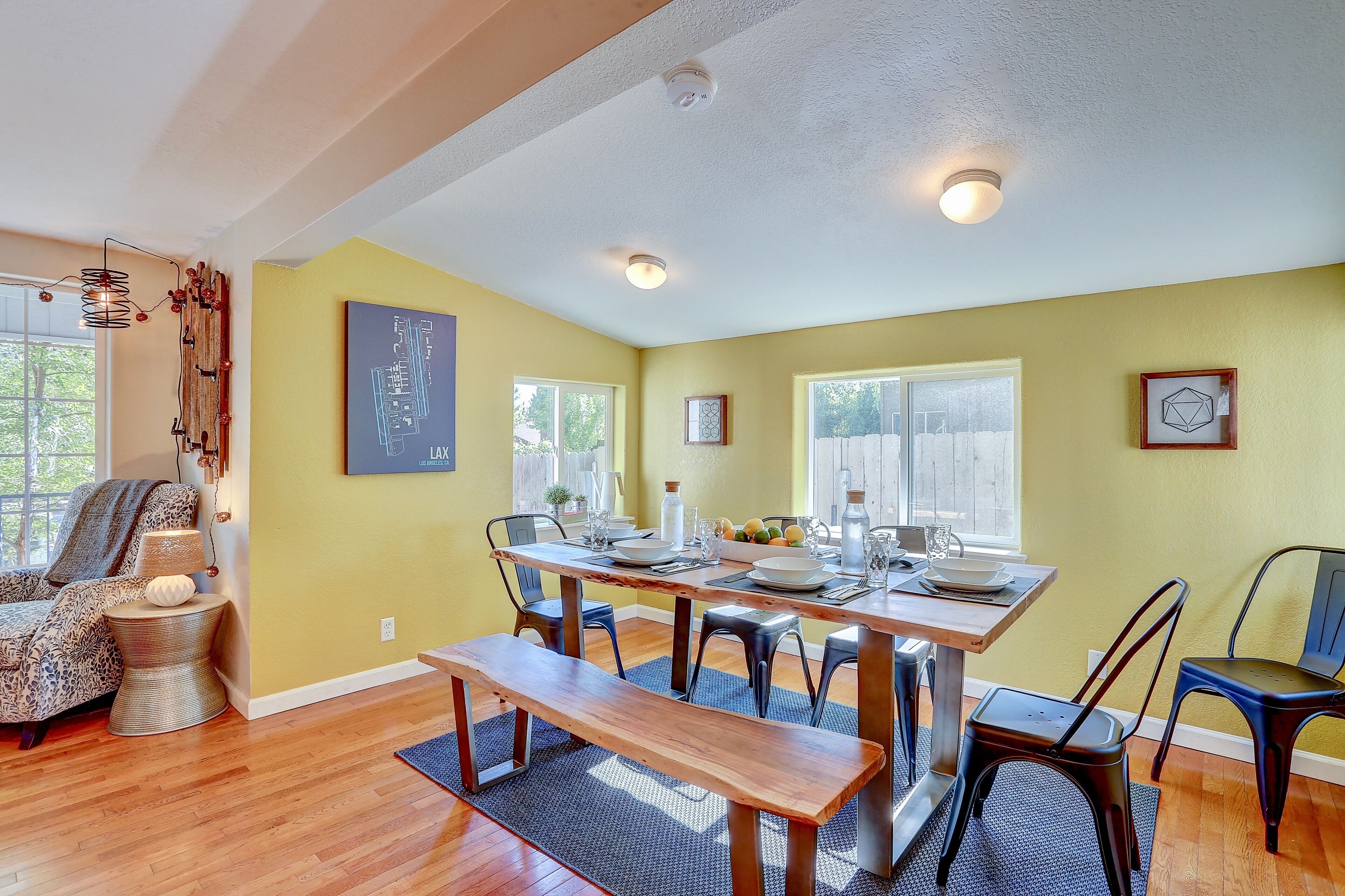 Un coin repas avec une table en bois dressée pour quatre personnes, entourée de chaises, d’un banc et d’une décoration murale.