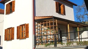 A two-story building with wooden shutters, a balcony with a metal railing, and a clear blue sky in the background. - Casa Sole - Vacation apartments on the Flower Riviera, decorated with love (Diano San Pietro)