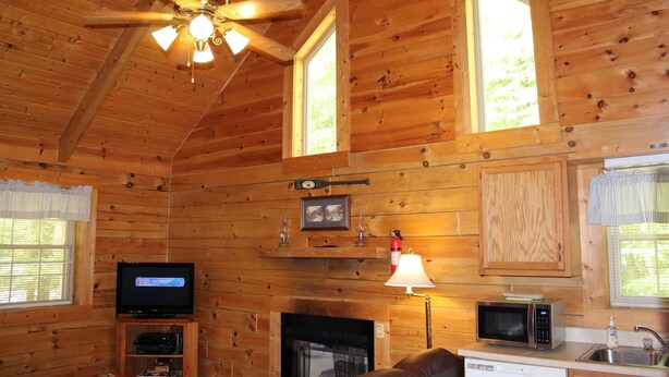 A wooden cabin interior with a fireplace, television, and kitchen area. - Mountaineer Relaxing 2 Bedroom Cabin  (Hico)