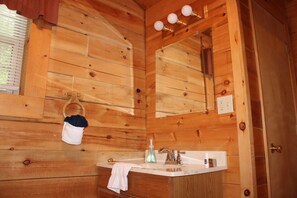 Bagno di una baita in legno con lavabo, specchio e pareti in legno.
