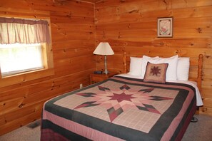 Una camera da letto in una casetta di legno, con un letto, un comodino, una lampada e una finestra con tende.