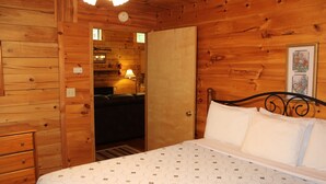 A wooden cabin-style bedroom with a bed, dresser, and a door leading to a bathroom. - Mountaineer Relaxing 2 Bedroom Cabin  (Hico)