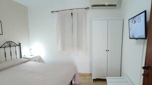 Een slaapkamer met een bed, een kledingkast, een nachtkastje en een airconditioning.