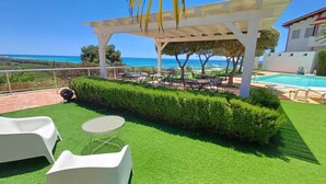 Een dakterras met kunstgras, witte lounge fauteuils, een ronde tafel en uitzicht op de oceaan.