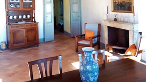 A spacious room with a wooden ceiling, a dining table with chairs, a blue vase, a fireplace with candles, and a painting on the wall. - Apartment - Silver Sunset (Manciano)