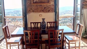 A dining area with a stone wall, a table, chairs, and a view of the countryside. - Apartment - Silver Sunset (Manciano)
