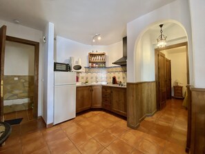 A kitchen with a white refrigerator, a microwave, and a stove. There is a wooden cabinet and a tiled backsplash.