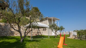 A stone wall, a white building with columns, and a grassy area with a slide.