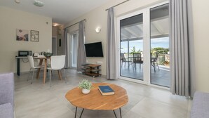 A modern living room with a dining area, a flat-screen TV, and a balcony with outdoor furniture.