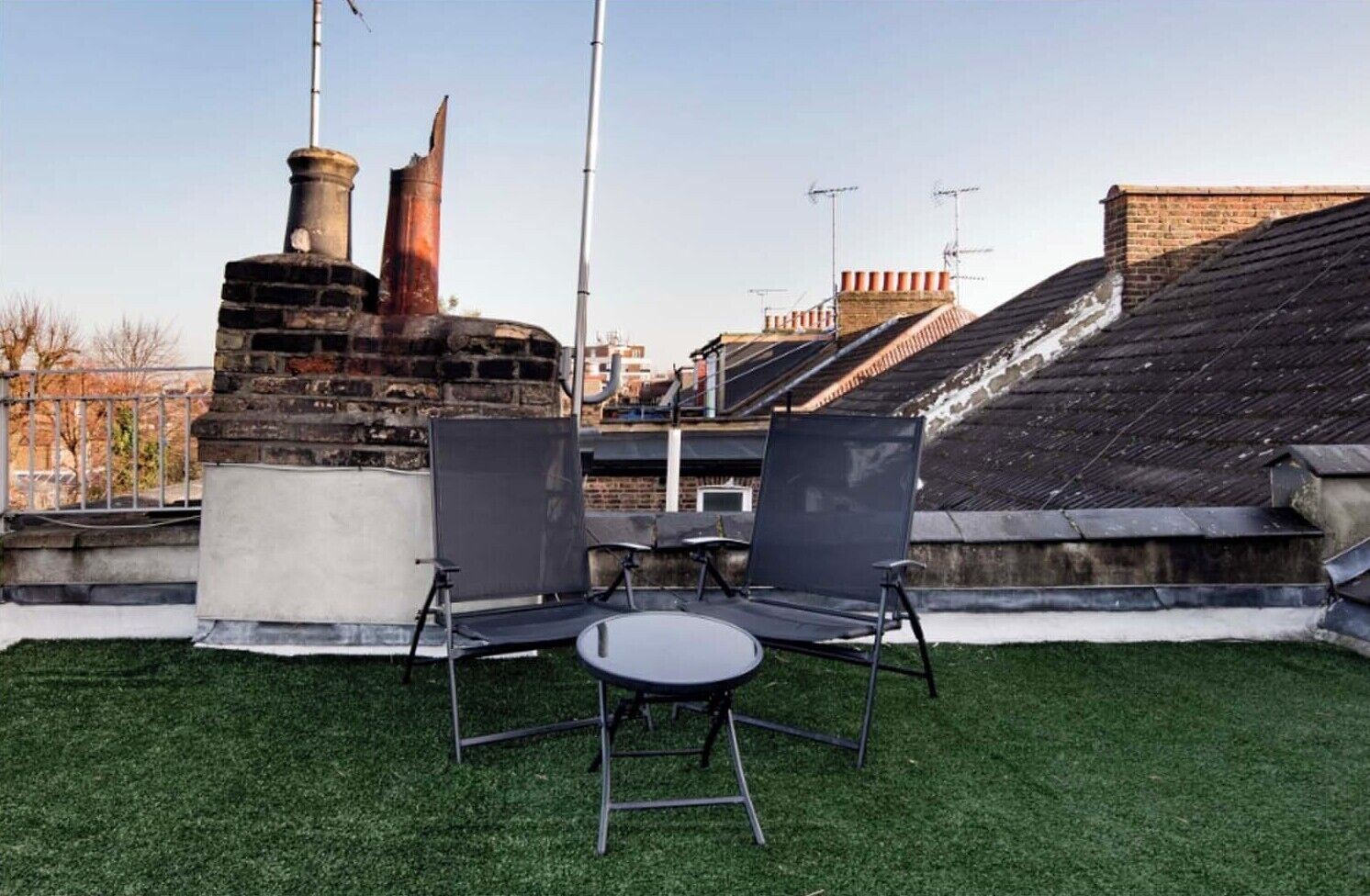 A rooftop terrace with a brick chimney, two chairs, and a small table.