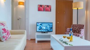 A living room with a TV, a sofa, a coffee table with drinks, and a door. - 3 Bedroom Pool Suite Sea View (Paxoi)