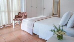 A bedroom with a bed, a chair, a bedside table with a vase of flowers, and a mirror on the wall. - 3 Bedroom Pool Suite Sea View (Paxoi)