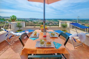A terrace with a table set for two, chairs, a table umbrella, and a view of the countryside.