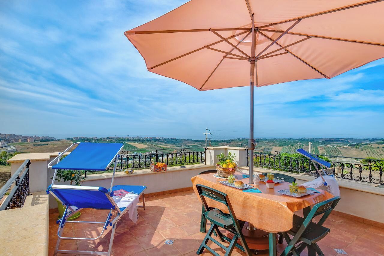 A terrace with a table and chairs, an umbrella, and a view of the countryside.