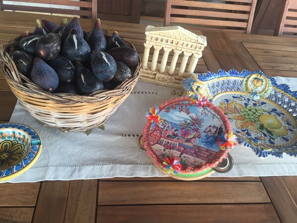 Une table sur laquelle se trouve un panier en osier rempli de figues, une petite maquette d’un bâtiment classique et deux assiettes décoratives ornées de motifs de fruits.