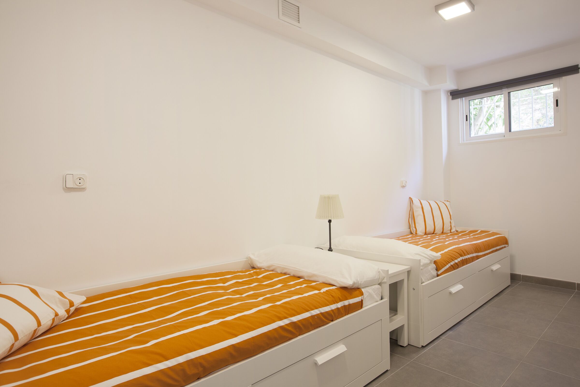 Een tweepersoonskamer met twee bedden, een raam en een witte muur.