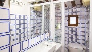 Une salle de bain avec un lavabo blanc, un miroir et des toilettes. Les murs sont recouverts de carreaux disposés selon un motif à carreaux bleus.