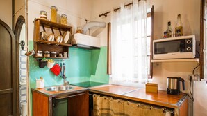 Une cuisine compacte équipée d’un évier, d’une cuisinière et d’un four à micro-ondes. On y trouve des étagères avec des bocaux et une fenêtre avec des rideaux.
