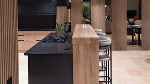 A modern kitchen with a central island, black countertops, and a wooden accent piece. - Villa Buse, wonderful sea view. (Kalkan)